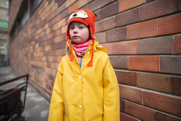 Little girl with Down syndrome looking at camera outoors in winter against brick wall.