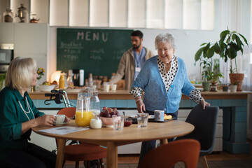 Smiling elderly women enjoying breakfast in nursing home care center.