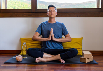 Handsome young adult male meditating in lotus flower posture with his hands doing namaste...