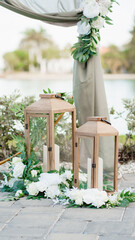 Wedding ceremony decoration with wooden lantern with a candle inside and a white bouquet of flowers Decorated area with white candle lamps and greenery Close up Wedding arch on the background	