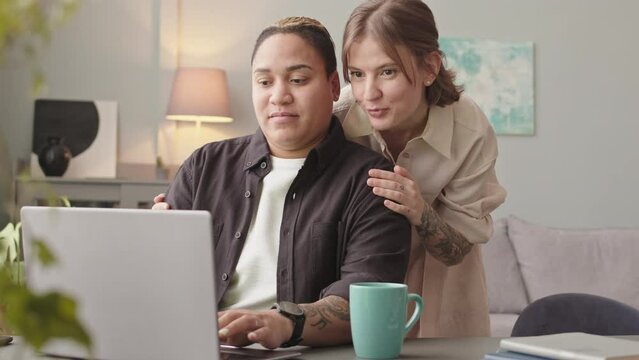 Waist up slowmo of Biracial lesbian woman using laptop while working from home showing results of her work to young beautiful wife
