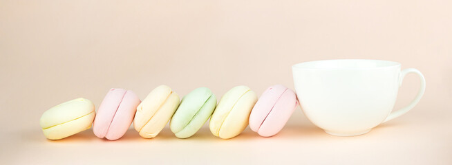 Obraz na płótnie Canvas Tasty sweet color marshmallows looks like macaron with porcelain white coffee cup mug on pastel beige background, Bakery concept.