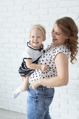 Mother holds her child with hearing aids and cochlear implants on white brick wall . Deaf and health concept