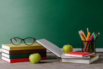 Set of stationery, eyeglasses and apples on table in classroom