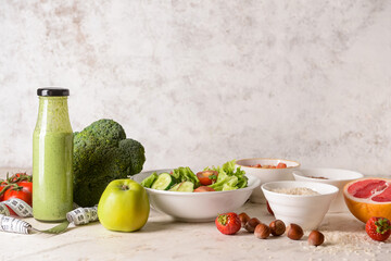 Different healthy products, bowl of salad, bottle of smoothie and measuring tape on light background