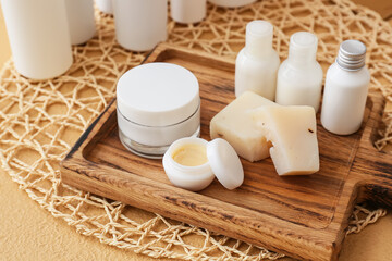 Wooden board with cosmetic products and soap on color background, closeup