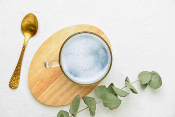 Wooden board with glass cup of delicious Charcoal Latte, spoon and eucalyptus branch on white table