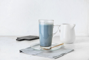 Glass cup of delicious Charcoal Latte, spoon and napkin on light background