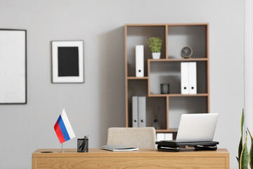 Workplace with modern laptop, notebook, stationery holder and Russian flag in light room