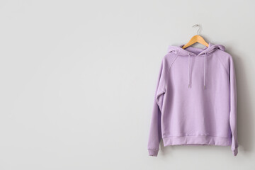 Stylish lilac hoodie hanging on light wall