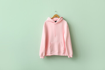 Stylish pink hoodie hanging on green wall