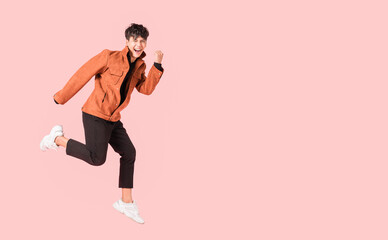 Happy handsome Asian man in fashionable clothing and jumping doing winner gesture isolated on pink background. - obrazy, fototapety, plakaty