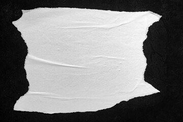 Obraz premium Sheet of white paper with torn edges on a black wall.
