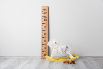 Big ruler for height measuring, rocking horse and wooden toy cars near light wall