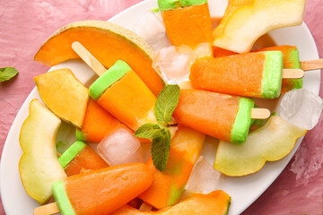 Plate with tasty popsicles and melon pieces on pink background