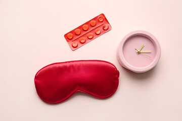 Sleep mask, pills and alarm clock on color background
