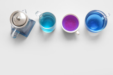 Teapot and cups of blue tea on light background