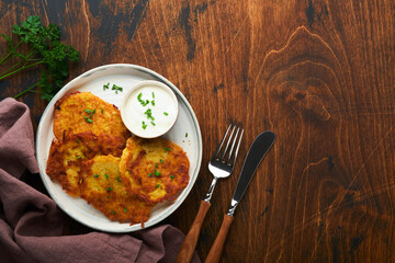 Potato pancakes. Fried homemade potato pancakes or latkes with cream and green onions in rustic plate on old wooden brawn table background. Rustic style. Healthy food. Top view.