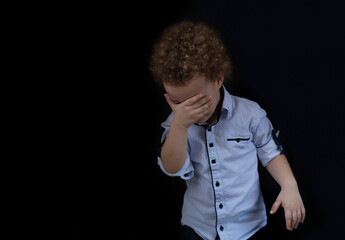 The boy covers his eyes with his hands