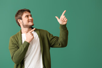 Handsome young man pointing at something on green background