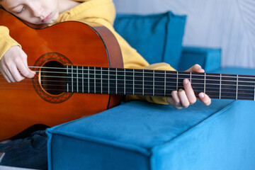 Close up hand of child playing acoustic guitar at home.