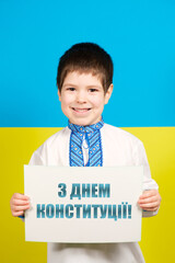 A happy boy of 4 years old smiles and holds a sheet with a text in Ukrainian, translation from Ukrainian - Happy Constitution Day.