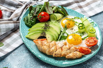 Fried egg. Close up view of the Chicken grilled fillet, fresh tomatoes, cucumbers, and avocado. Ketogenic diet breakfast. Food recipe background