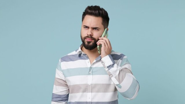 Perplexed angry sad young bearded brunet man 20s years old wears striped shirt talk on mobile cell phone ask what bad news scream swear isolated on plain pastel light blue background studio portrait