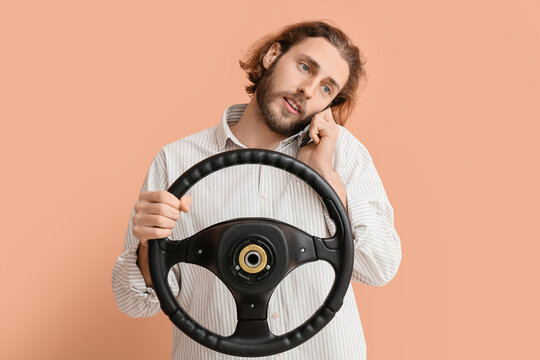 Handsome man with steering wheel talking by phone on color background