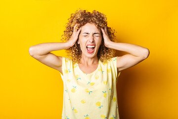 screaming young girl in shock holding her head with her hands on yellow background.
