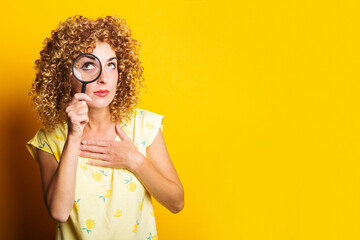 curly-haired girl looks up through a magnifying glass on a yellow background.