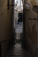 Stairs on a very narrow street with a man with a mask walking.