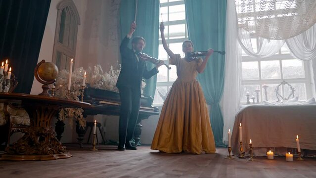 A Young Girl And Man Plays The Violin In A Beautiful Retro Room With Flowers And A Piano.