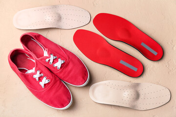 Pair of shoes and orthopedic insoles on color background