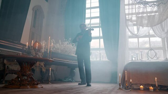 A Young Girl And Man Plays The Violin In A Beautiful Retro Room With Flowers And A Piano.