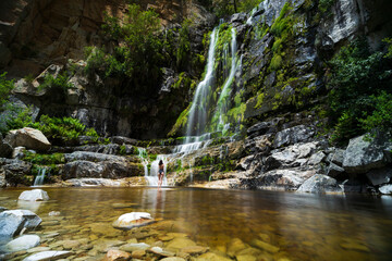 View of a woman standing in front of a waterfall in black swimsuit, Rawsonville, Western Cape, South Africa.