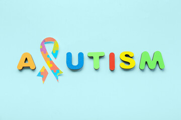 Word AUTISM with paper awareness ribbon on blue background