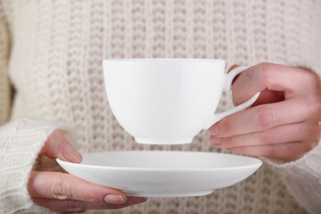 Fototapeta na wymiar Tea in a white cup in a female hand on the background of a knitted sweater. White cup in female hands. Elegant female hands holding a white cup for coffee.
