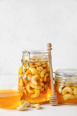 Jars with tasty cashew nuts in sweet honey on light background