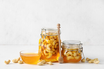 Jars with tasty cashew nuts in sweet honey on light background