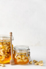 Jars with tasty cashew nuts in sweet honey on light background