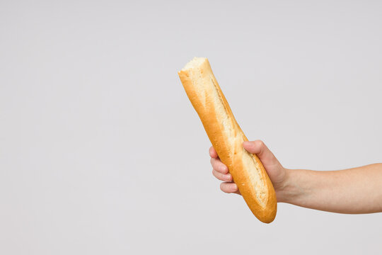 bitten baguette bread in a female hand on a white background close-up