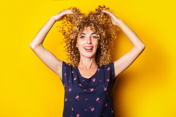 cheerful curly young woman lifts her hair up on a yellow background