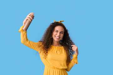 Pretty young African-American woman with hair spray on blue background