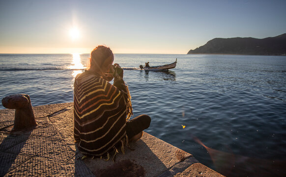 View of a beautiful woman shooting photographs on the pier at sunset along the coast, Vernazza, Cinque Terre, Liguria, Italy.