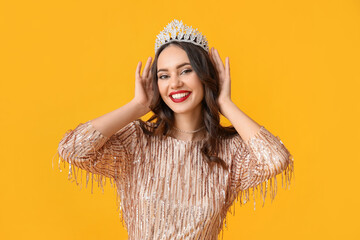 Beautiful young woman in stylish dress and tiara on yellow background