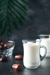 Ramadan Kareem food and drinks. Plate of dates, glass of milk and date palm branch on black background. Righteous Muslim Lifestyle. Vegetarian food. Selective focus.