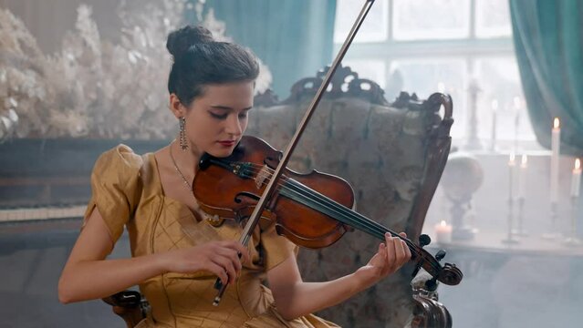 A Young Girl And Man Plays The Violin In A Beautiful Retro Room With Flowers And A Piano.