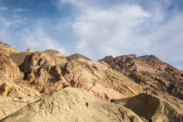 Man Climbs Rugged Desert Mountains with Blue Sky and Clouds Landscape