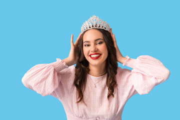 Beautiful happy young woman in stylish dress and tiara on blue background